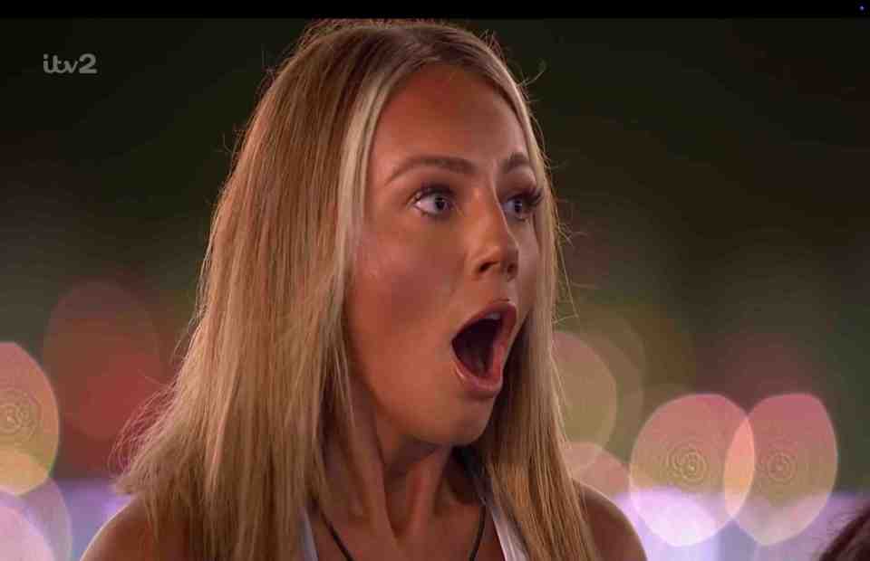 A shocked woman watches on a large screen.