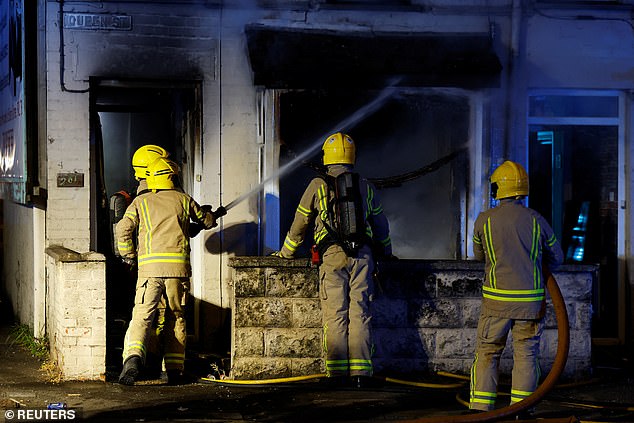 Firefighters work to extinguish a fire started by protesters in a house during a second night of riots