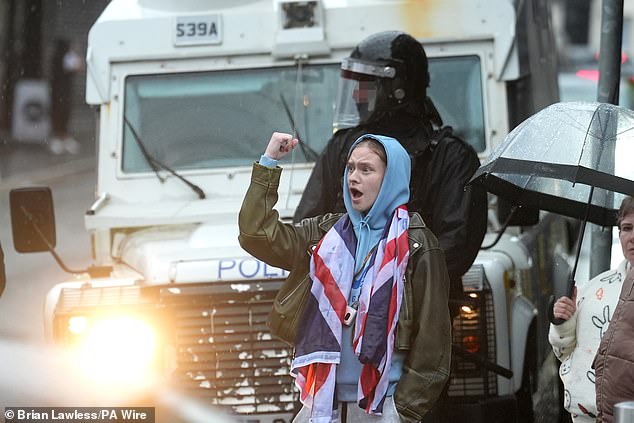 A person wears a Union Jack flag and stands near armed police in Portadown on Thursday