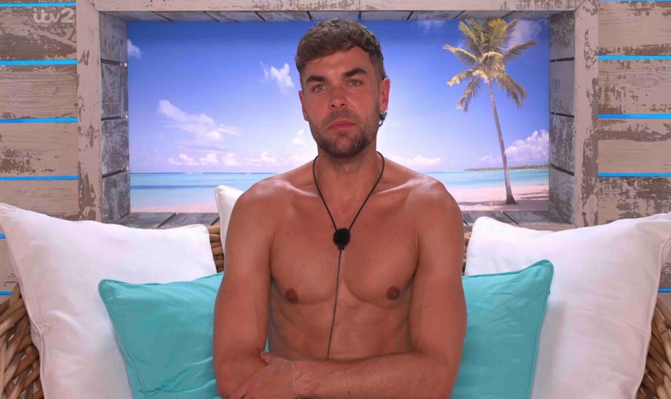 Shirtless man sitting on a couch in front of a beach scene.