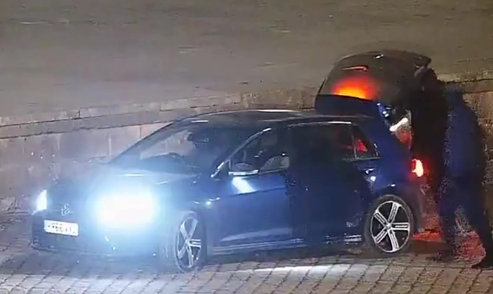 Surveillance image of a blue car with its trunk open at night.