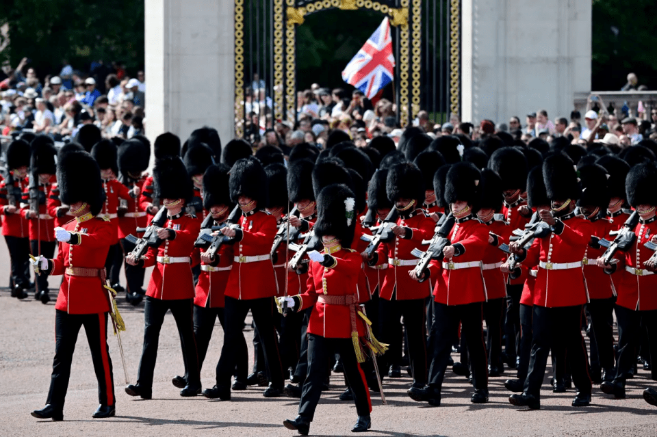 Soldiers in red tunics and bearskin hats marching.