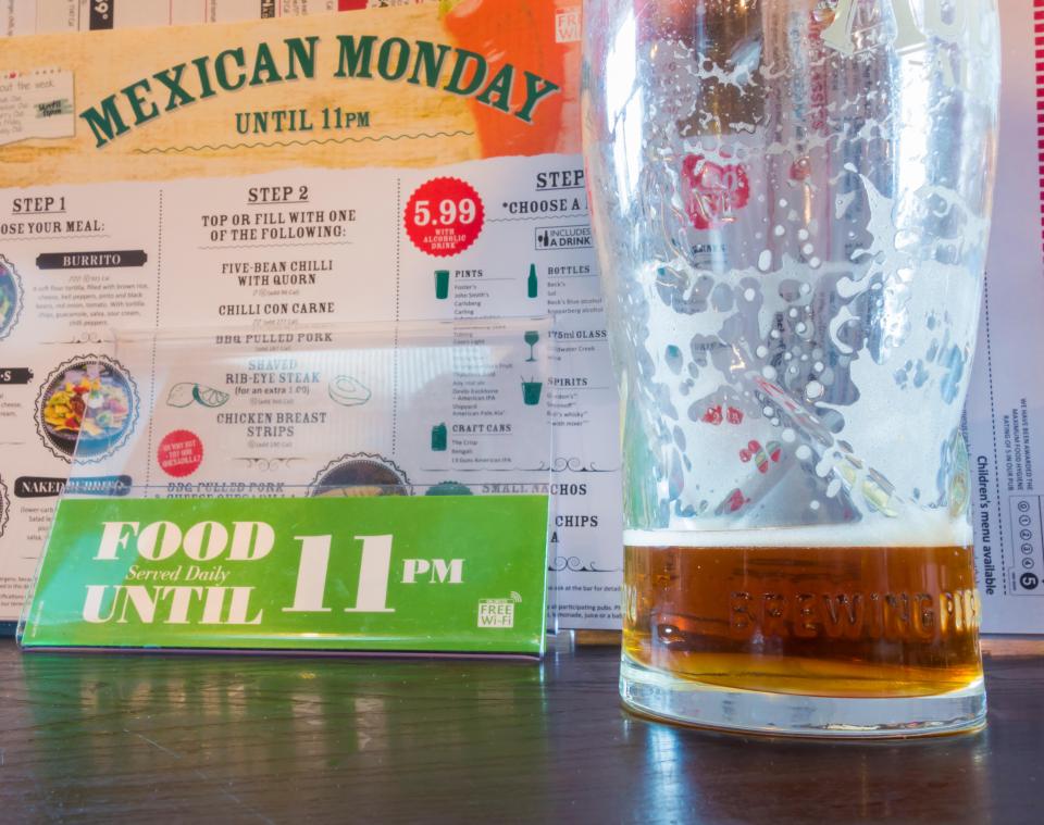 A pint of beer sits on a table next to a menu advertising Mexican Monday specials.