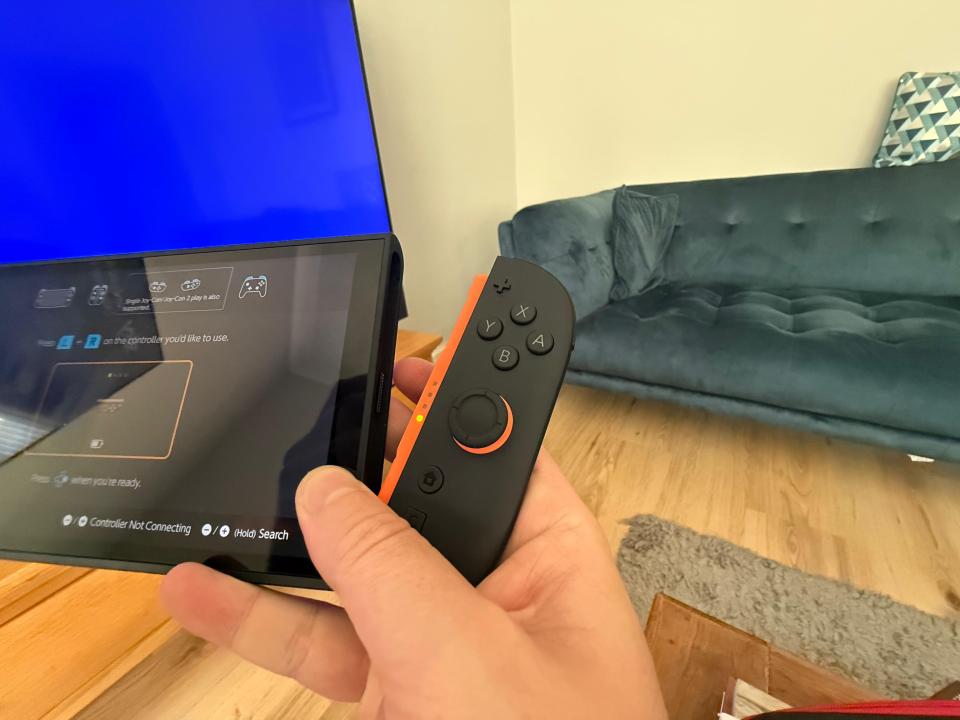 Hand holding a video game controller, attempting to connect to a device displaying a connection screen.
