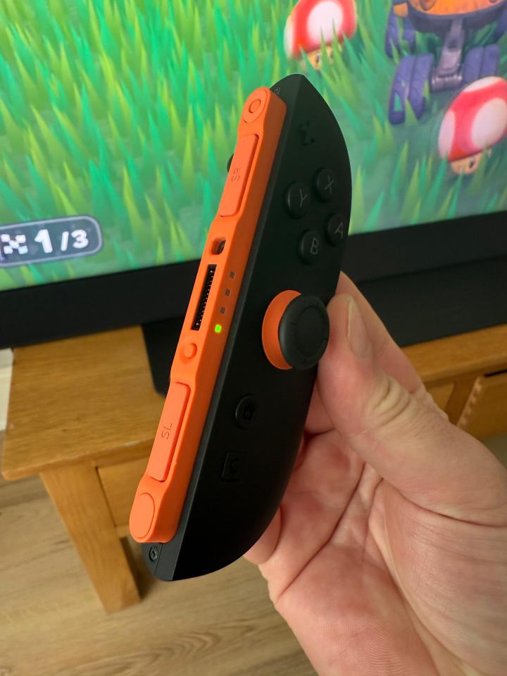 Hand holding a black and orange video game controller.