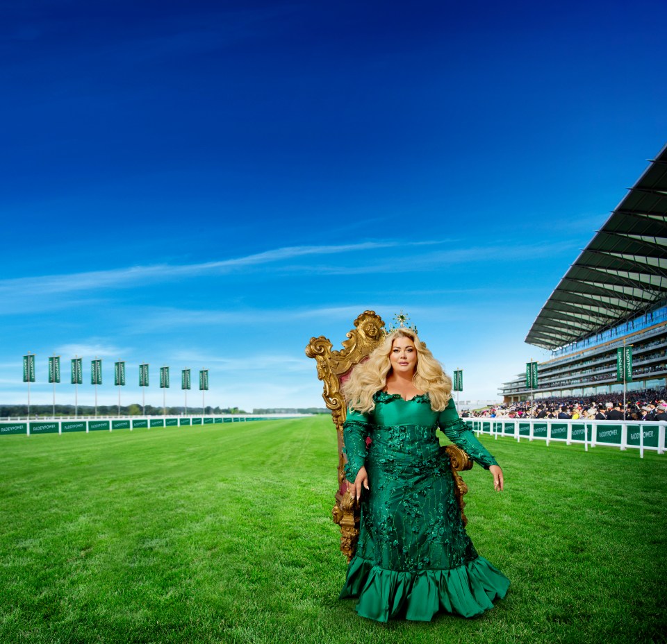 Woman in green dress seated on a throne on a racecourse.