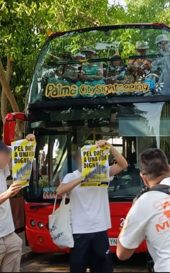 Protestors blocking a sightseeing bus in Palma, holding signs demanding a dignified life.
