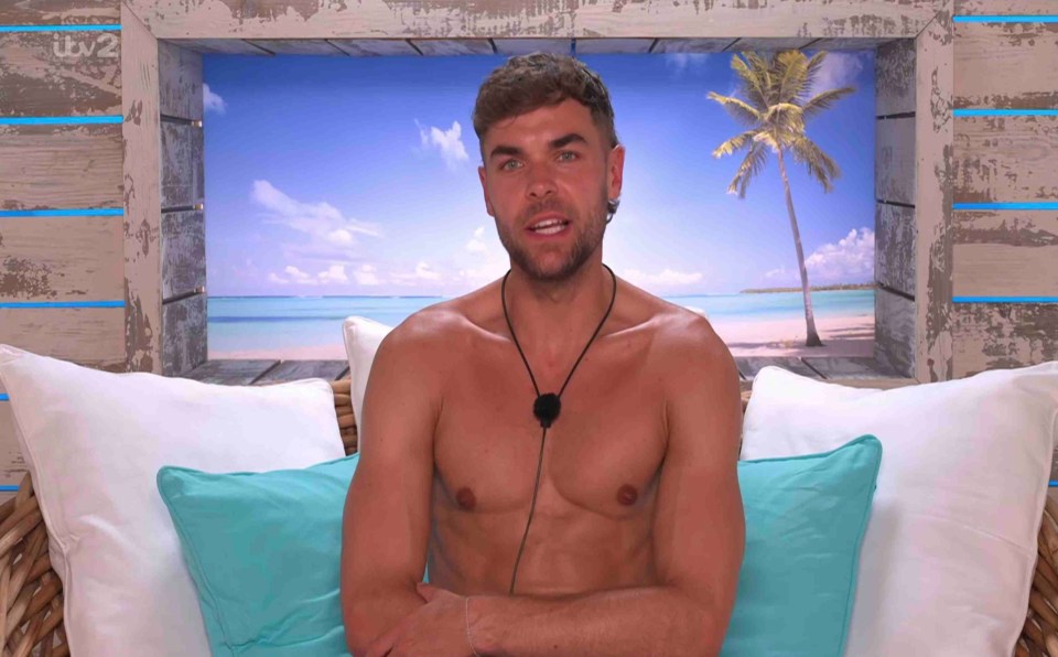 Shirtless man sitting on a couch in front of a tropical beach scene.