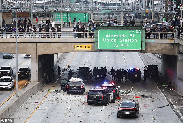 Police officers take cover as activists shower rocks and debris onto their vehicles during protests sparked by immigration raids in LA Sunday