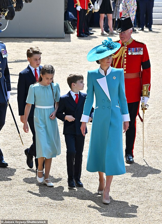 Kate leads her children into Buckingham Palace to prepare for the balcony appearance. She is wearing a coat dress by Catherine Walker