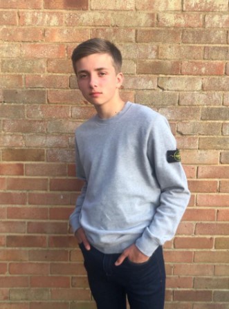 Teenage boy in grey sweatshirt standing against brick wall.