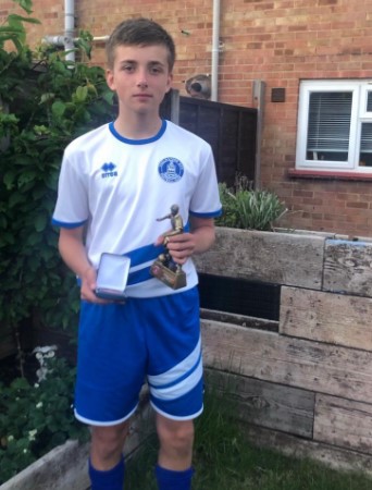 Boy in soccer uniform holding award and medal.