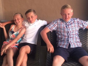 Three children sitting on patio chairs.