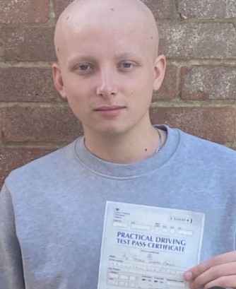 A young man with a shaved head holds up his driving test pass certificate.