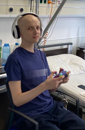A young man with a shaved head plays a video game in a hospital room.