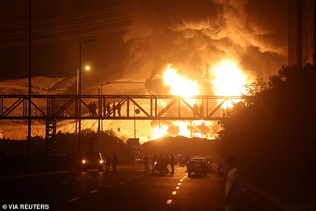 People watch from a bridge as flames from an Israeli attack rise from Sharan Oil depot, following Israeli strikes on Iran, in Tehran, Iran, June 15, 2025