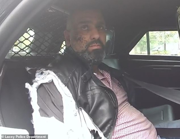Ihsan in police bodycam footage sitting a patrol car. His jacket was torn in the struggle and dirt pressed into one side of his face during the attack