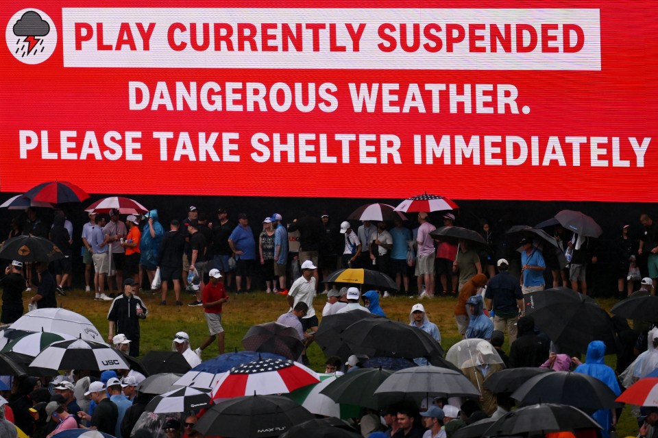 Large sign announcing play suspension due to dangerous weather, urging immediate shelter; spectators seeking cover under umbrellas.