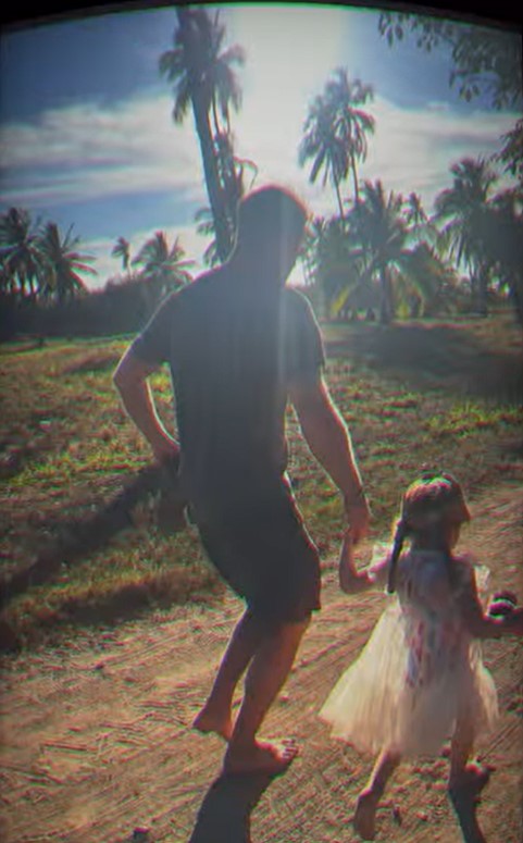 Man and child holding hands walking on a dirt road.