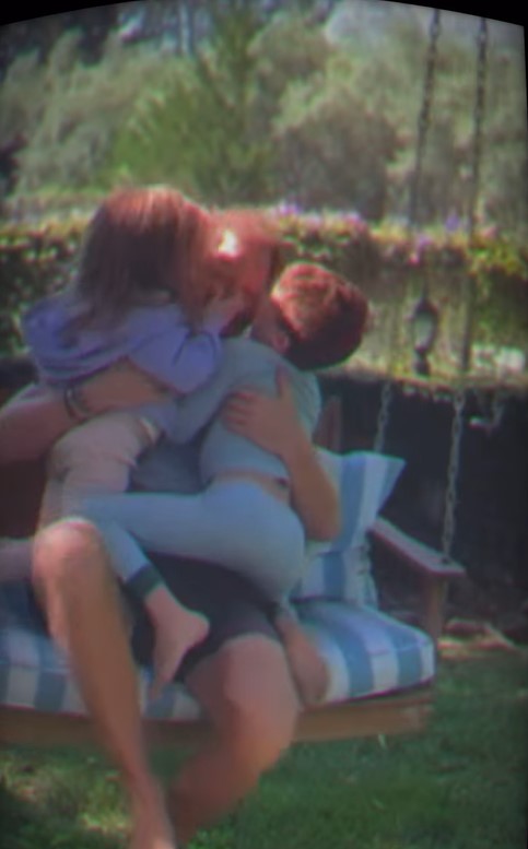Man embracing his two children on a swing.