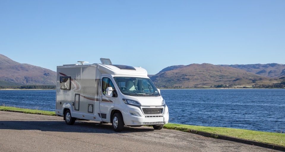 Motorhome parked by a lake with mountains in the background.