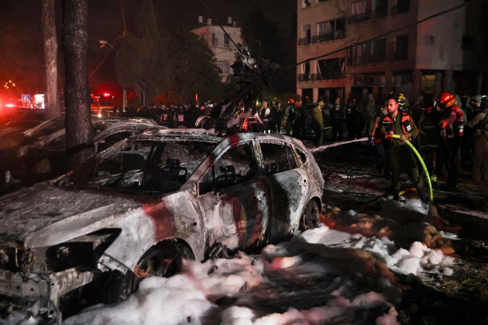 Emergency personnel extinguishing a fire in a damaged car after a missile attack.