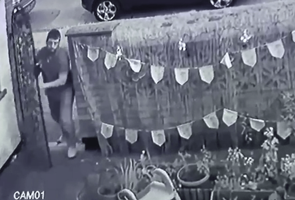 Black and white security camera footage of a man entering a gate.
