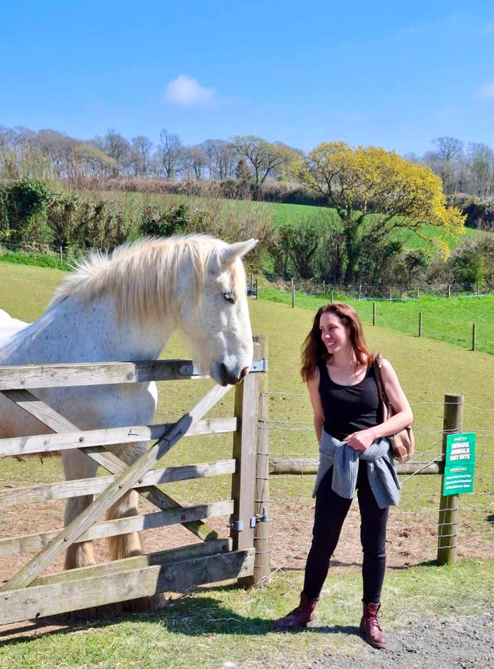 Woman looking at a white horse through a wooden fence.