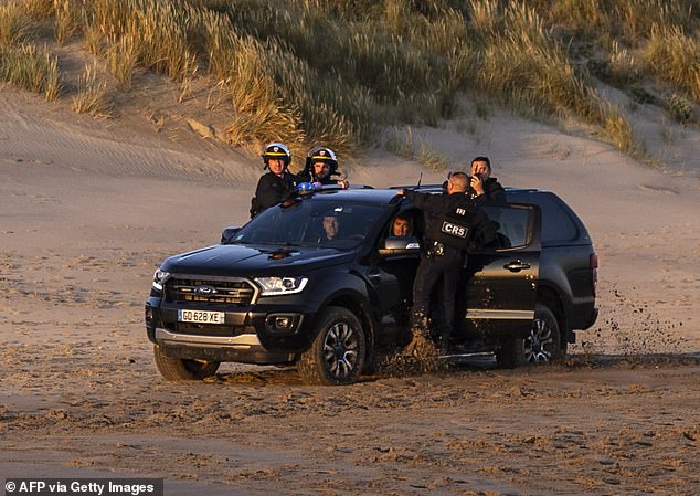 French Republican Security Corps (CRS - Compagnies Republicaines de Securite) officers drive as migrants walk in the water