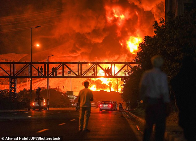Iranians looking as a plume of heavy smoke and fire rise from an oil refinery in Tehran, after it was hit in an overnight Israeli strike