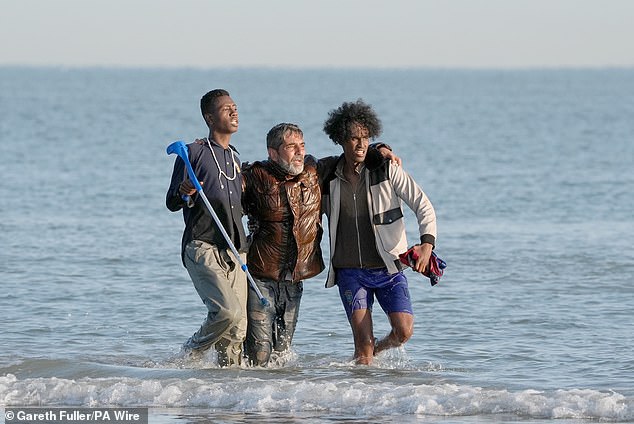 People thought to be migrants wade through the sea to board a small boat leaving the beach at Gravelines