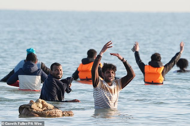 People thought to be migrants wade through the sea to board a small boat leaving the beach at Gravelines