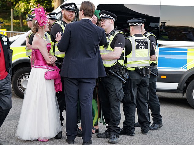 A man donning a suit and a woman in a pink and white summer dress speaking to police officers