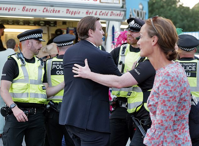 The man in a suit is seen being handled by one of the police officers