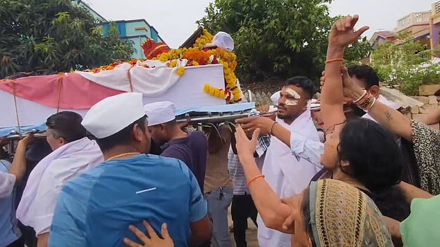Another mourner appears to try to help him to carry the coffin, but the grieving man refuses