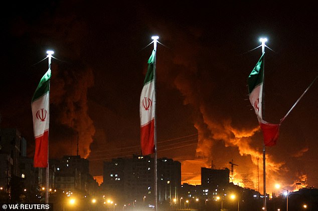Reza Pahlavi has called on Iranians to rise up against Khamenei's regime. (Pictured: Iranian flags fly as fire and smoke from an Israeli attack on Sharan Oil depot rise)