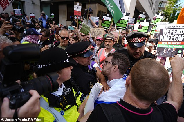 Police officers remove a counter-protester from the middle of supporters of Kneecap today