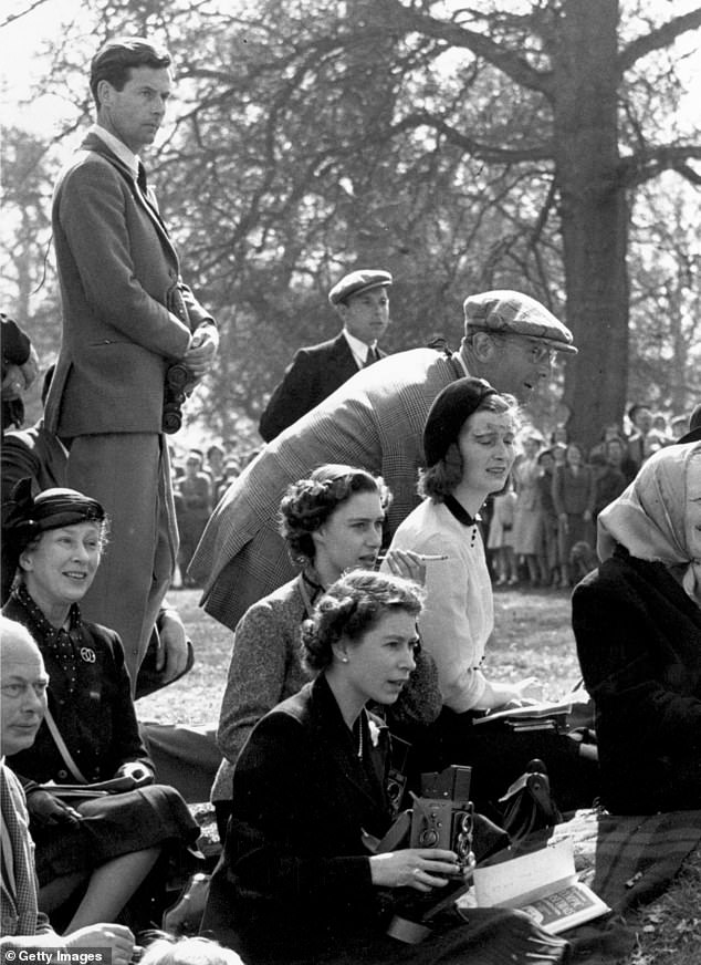 Queen Elizabeth holds a camera at the 1955 Olympic Horse Trials with her sister sat behind her smoking a cigarette and Peter stood further back