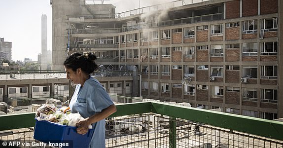 A nurse carries medical supplies past a building with smoke billowing out after at Soroka Hospital after it was struck by an Iranian missile in Beersheba in southern Israel on June 19, 2025. Soroka Hospital and two towns near Tel Aviv were struck after a barrage of Iranian missiles early on June 19, with rescuers reporting at least 47 people injured in the latest attacks. (Photo by JOHN WESSELS / AFP) (Photo by JOHN WESSELS/AFP via Getty Images)