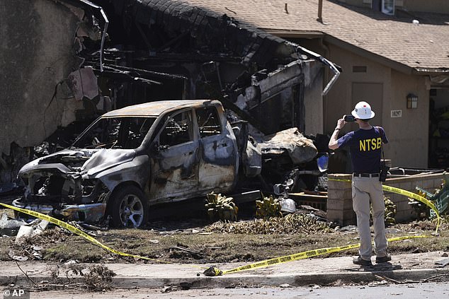 An NTSB worker takes photos of a vehicle and home that were damaged when a small plane crashed into a San Diego neighborhood on May 22, 2025