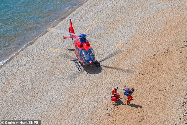 Air Ambulance workers exit the helicopter and walk along the beach as they respond to reports of a woman in need of urgent medical attention