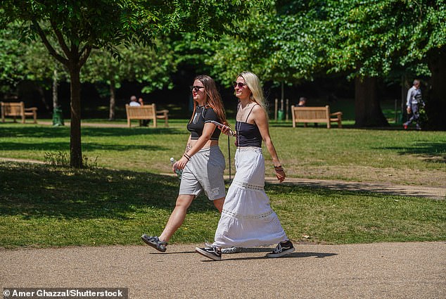Two women walk in the sunshine at St James's Park in London today as the heat continues