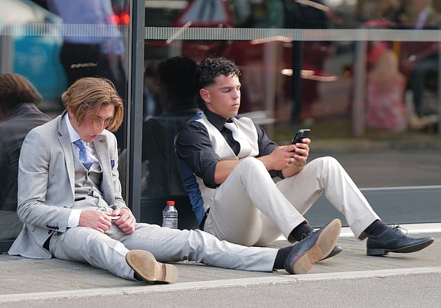 Two young men in suits rest up on the kerb with a bottle of water to re-hydrate