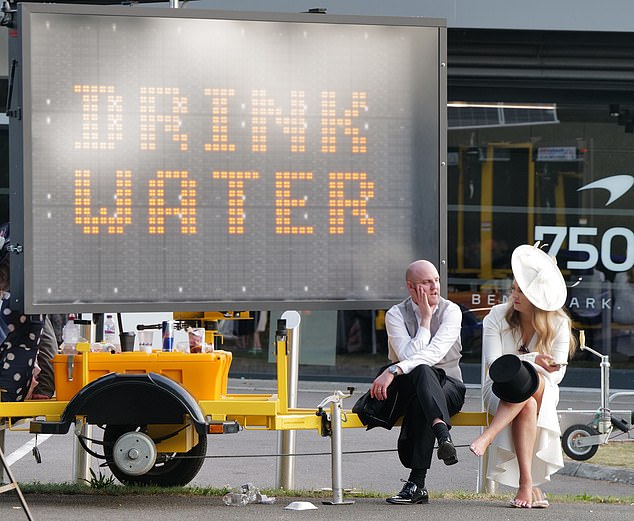 A couple sit by a sign with some handy advice to those enjoying their day in the sun