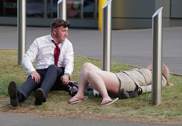 One man with his tie loosened and jacket removed watches on as a lady takes a lie down