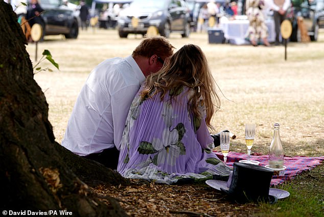 Hats off! One pair have popped open a bottle of bubbly to kick off the event as they relax on the racecourse grounds