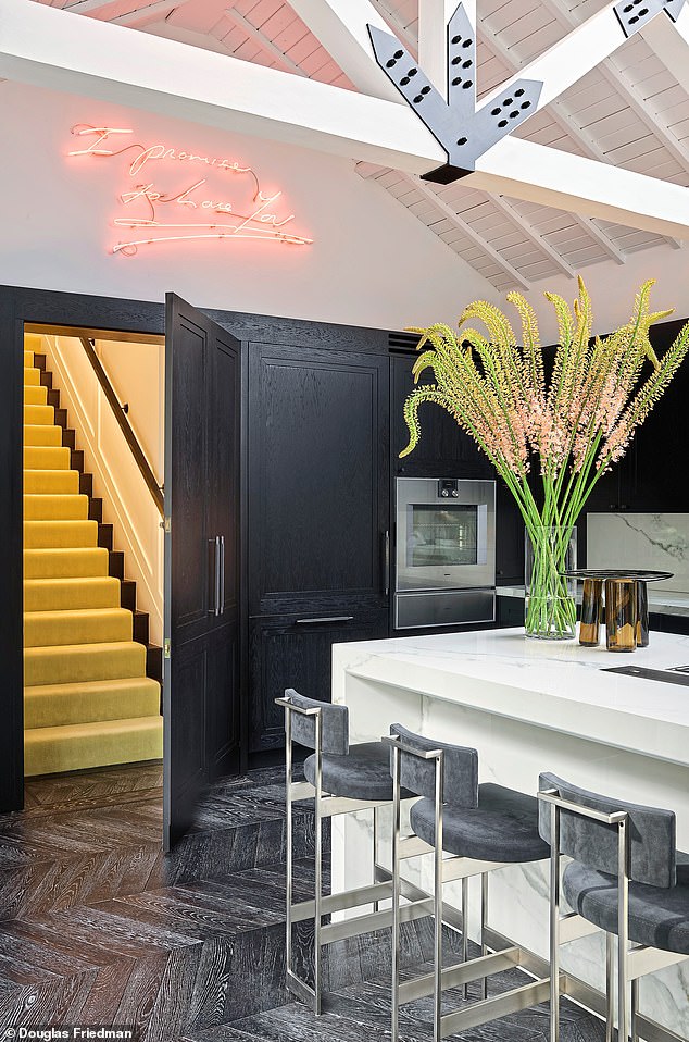A neon artwork by Tracey Emin hangs above a hidden stairway to the master suite, accessible only through this secret door in the kitchen, one of Forbes’ favourite spaces in the house.