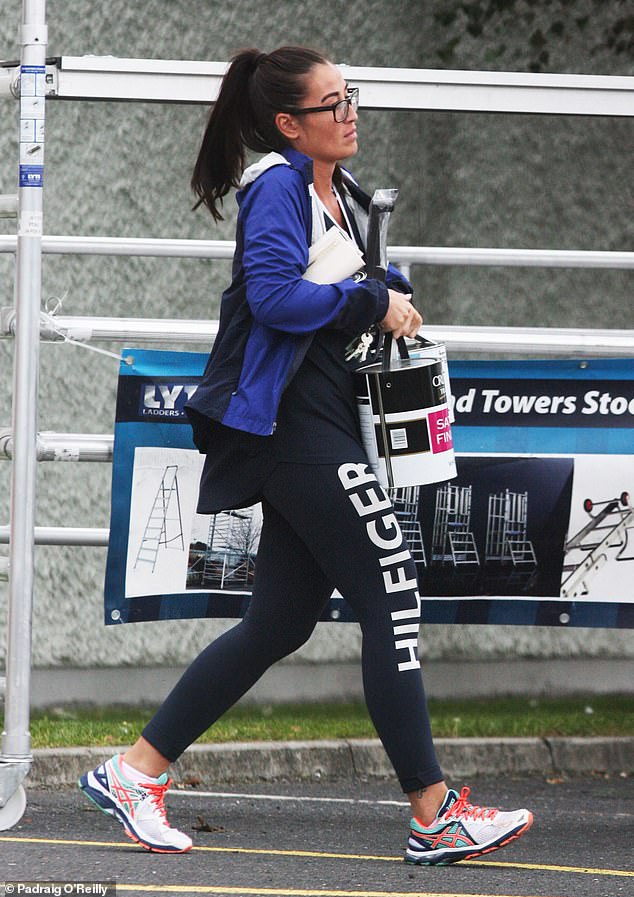 Charlene Lam in a pair of running shoes and designer leggings while holding what appears to be two vats of paint