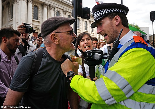 An activist clashes with a police officer who can be seen filming him amid the protest