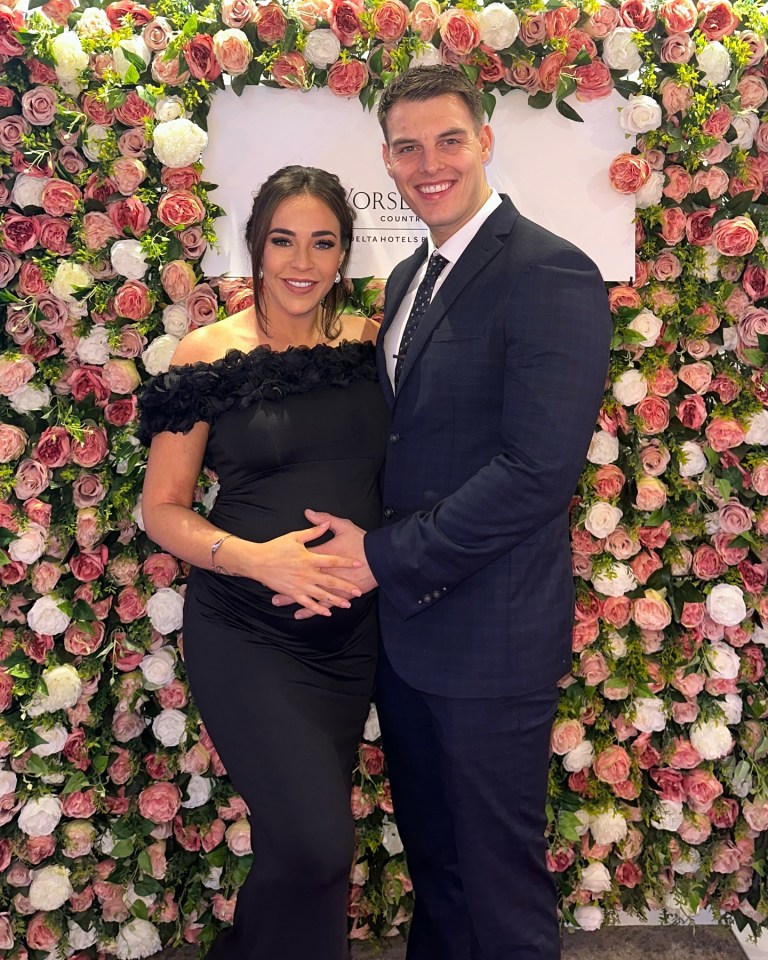 Pregnant Stephanie Davis and her partner posing in front of a flower wall.